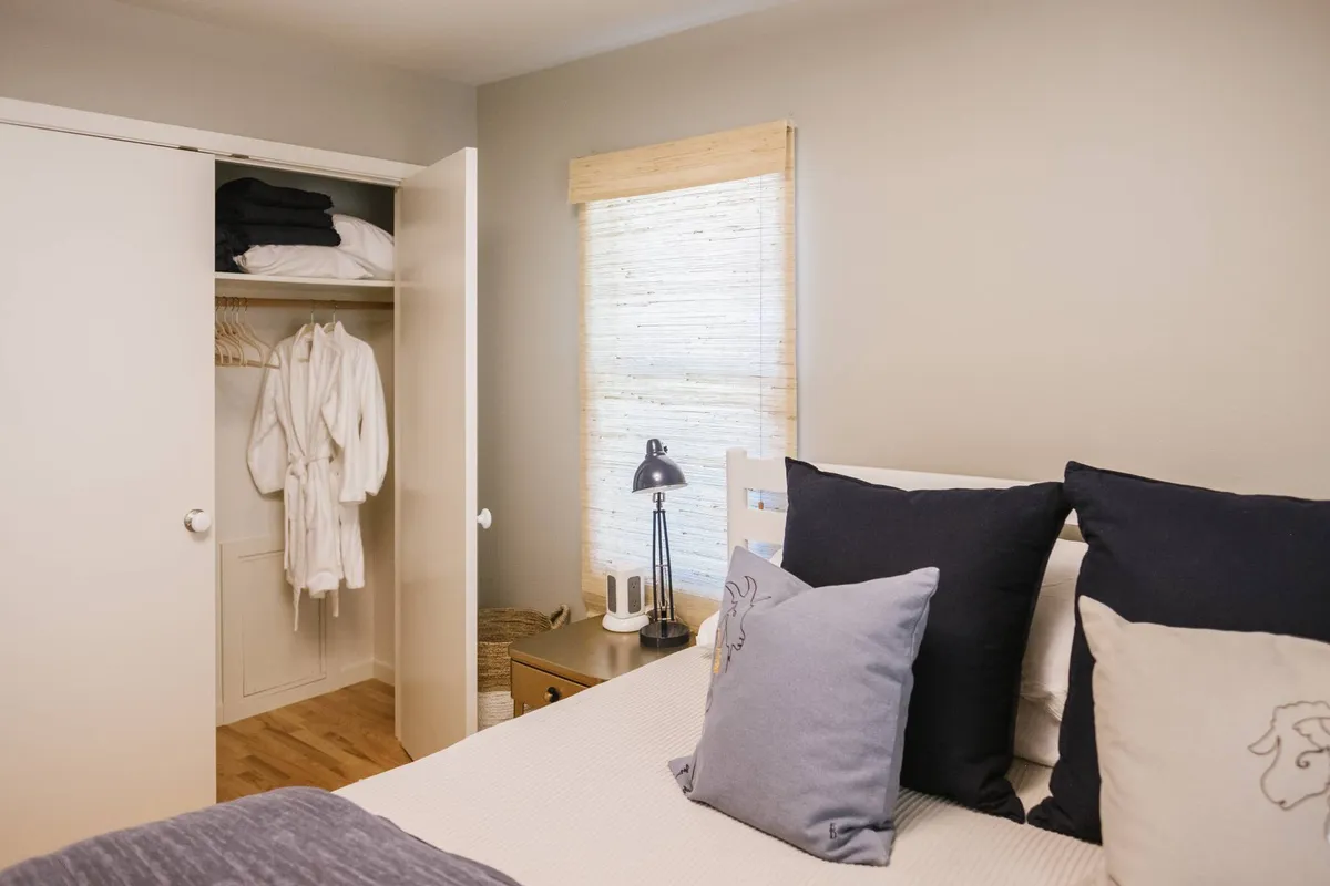 A tastefully arranged bedroom featuring a bed with decorative pillows, a closet with plush robes visible, and a window allowing in natural light. The scene exudes comfort and relaxation, suggesting both restful nights and convenient storage for extended stays.
