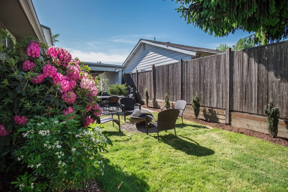The image features a tranquil patio surrounded by colorful flowers, with comfortable seating and a fire pit. The setting evokes the leisurely enjoyment of morning coffee or evening relaxation amid the blooms.