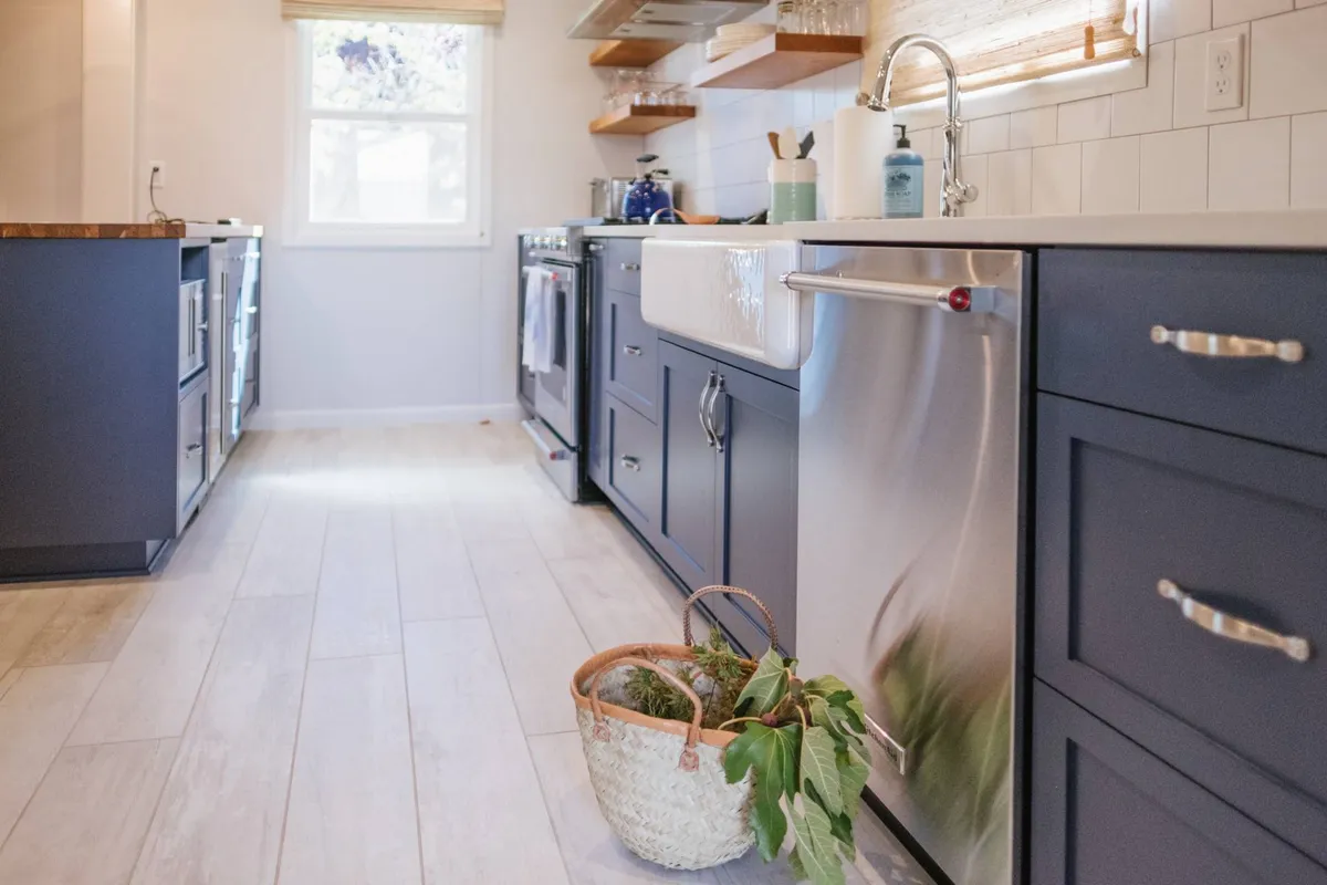 A welcoming kitchen featuring a large farmhouse sink, stainless steel appliances, open shelving with glassware, and a potted plant. The space is ideal for cooking, entertaining, and gathering with family or friends.