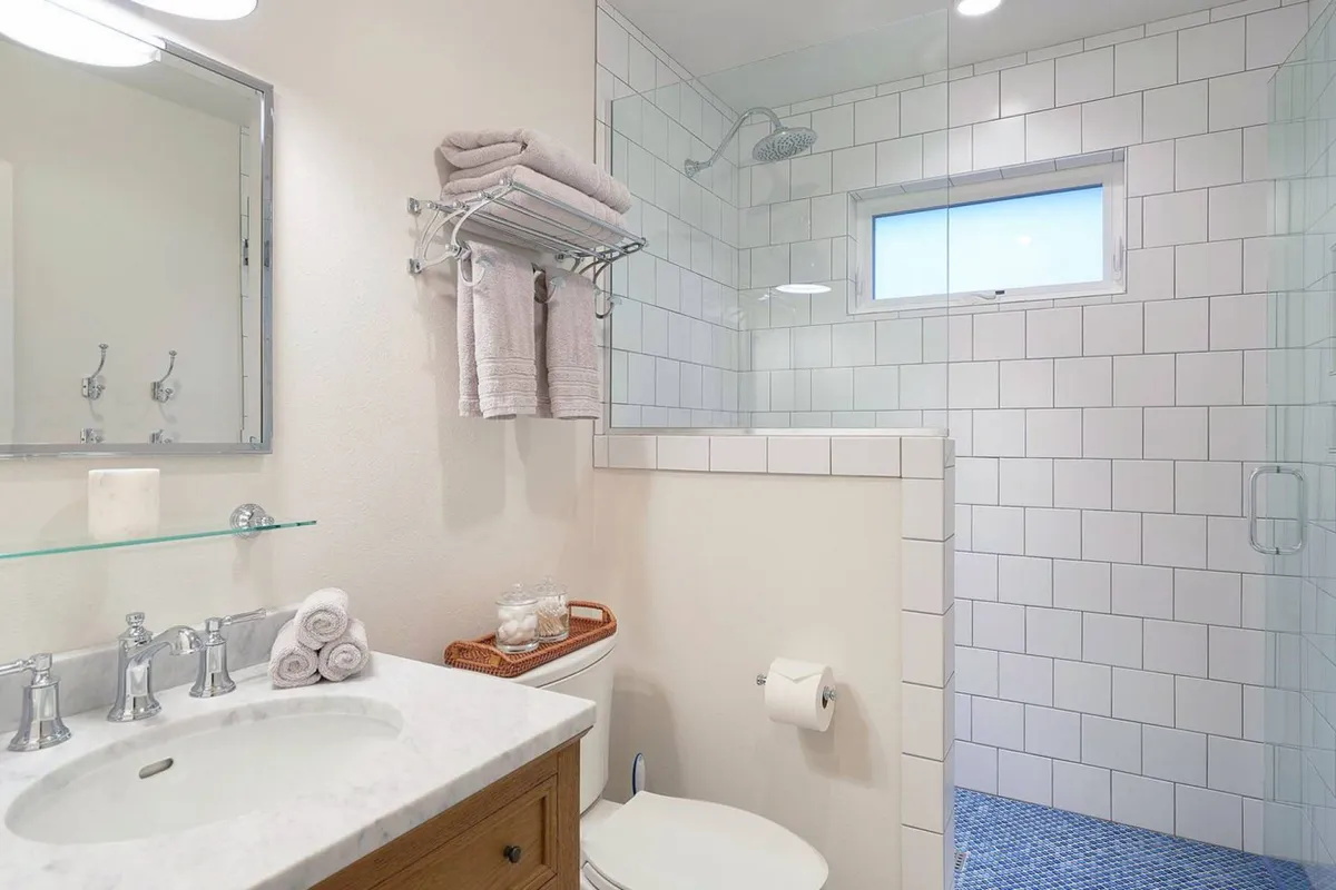 A modern, spa-inspired bathroom with a marble-topped vanity, a large walk-in rain shower, and an expansive mirror. The space is bright and airy, with soft lighting and fluffy towels, evoking a sense of privacy and rejuvenation.
