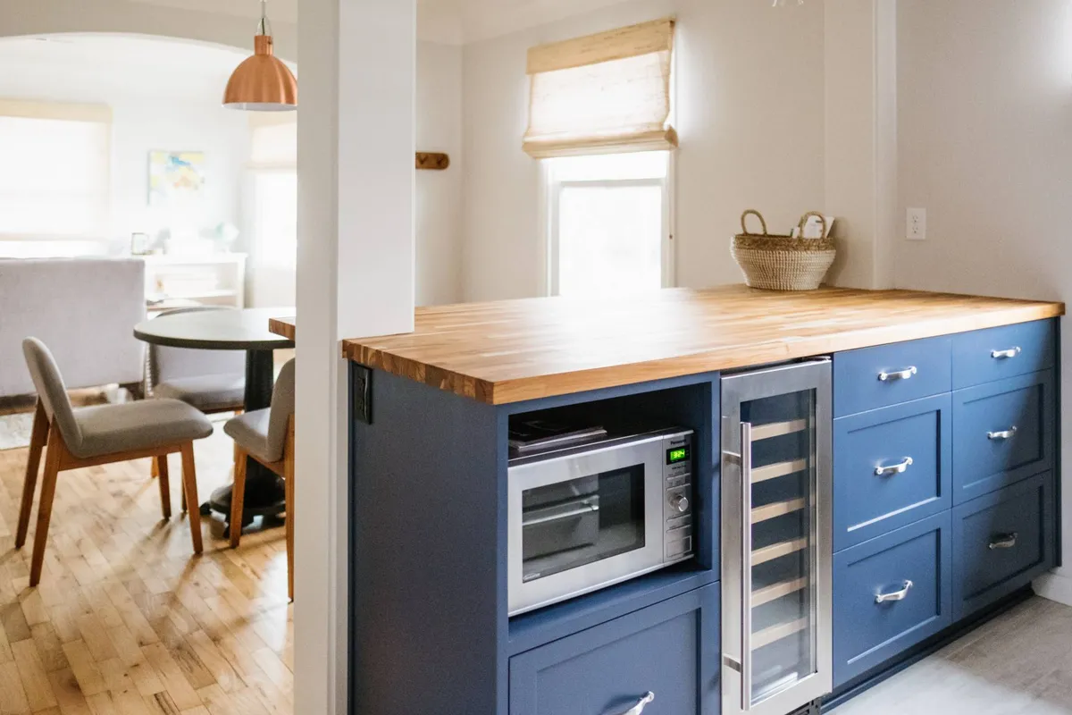 A modern kitchen setup with blue cabinetry, a wooden countertop, a visible wine cooler, microwave, and a kitchen table set for meals. The space feels inviting, ready for both cooking and entertaining.